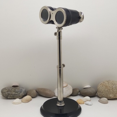 Binóculos antigos em suporte metálico com base preta, rodeados por pedras e conchas.