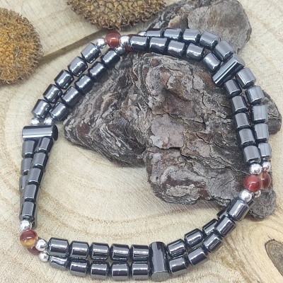 Pulseira preta e prateada com contas vermelhas sobre madeira e casca