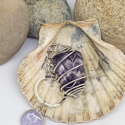 Chaveiro de pedra roxa e pendente PISCIS numa concha com pedras ao fundo