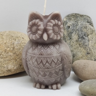 Vela castanha em forma de coruja com padrões geométricos, rodeada por pedras lisas