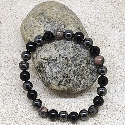 Pulseira de contas em preto, cinzento e castanho sobre pedra em areia