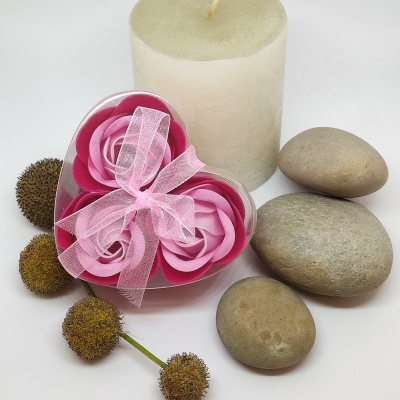 Conjunto decorativo com vela branca, pedras cinzentas, flores artificiais rosas em caixa coração com laço rosa e flores secas marrons