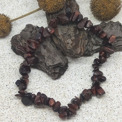Pulseira de pedras castanho-avermelhadas sobre casca de árvore e flores secas