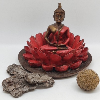 Estátua de Buda dourada com roupa vermelha numa base de lótus vermelha com cascas de árvore e bola texturizada