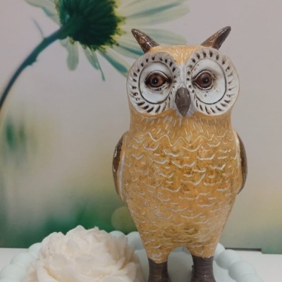 Estátua de coruja amarela e castanha em base branca com flor decorativa.