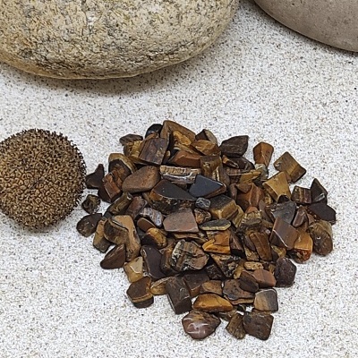 Pequenas pedras polidas castanhas e pretas com bola espinhosa e pedras cinzentas sobre areia clara