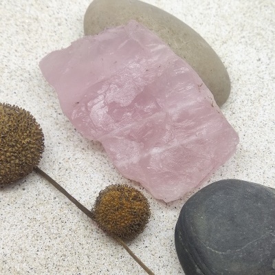Pedra de quartzo rosa e pedras lisas sobre areia clara com frutos secos castanhos
