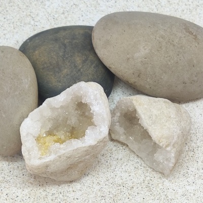 Pedras lisas cinza e geodas abertas com cristais em superfície clara