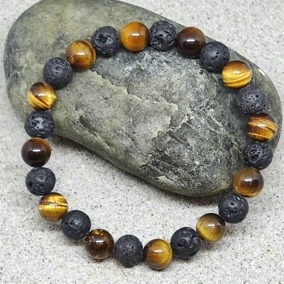 Pulseira com contas castanhas e negras porosas sobre pedra verde e fundo arenoso