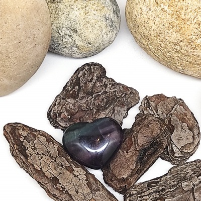 Coração de pedra polida azul e verde sobre cascas de árvore e pedras claras.