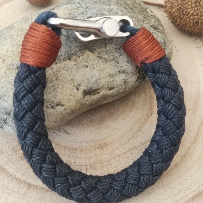 Pulseira trançada azul escura com fecho metálico sobre pedra e fundo de madeira