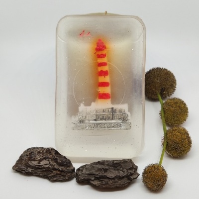 Vela com figura de farol e elementos naturais ao redor sobre fundo branco