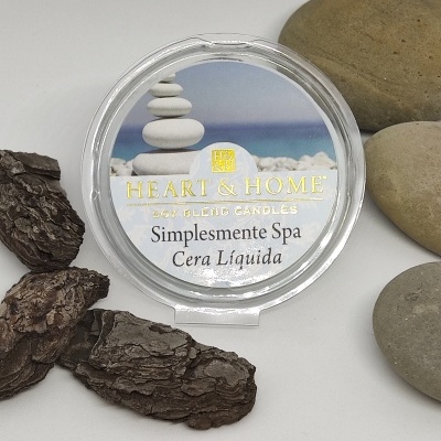 Vela em recipiente redondo transparente com tampa, texto 'Heart & Home Wax Blend Candles Simplesmente Spa Cera Líquida', rodeada por casca e pedras
