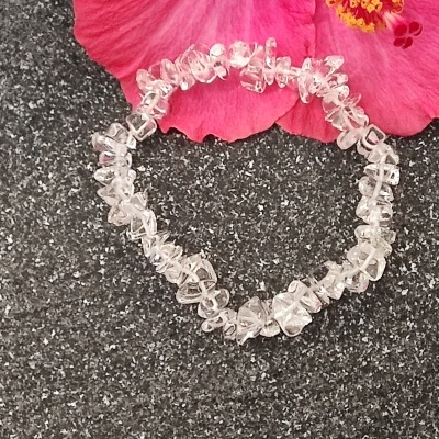 Pulseira de pedras transparentes sobre superfície preta ao lado de flor rosa