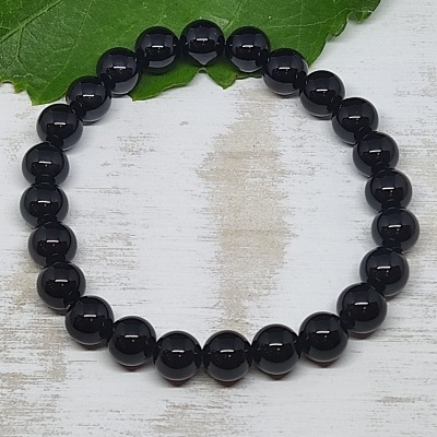 Pulseira de contas pretas brilhantes sobre superfície branca com folha verde