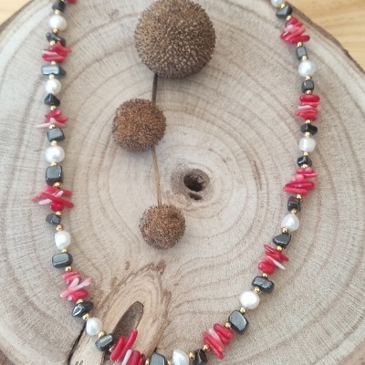 Colar de pedras coral, pérolas brancas e contas metálicas sobre suporte de madeira redonda