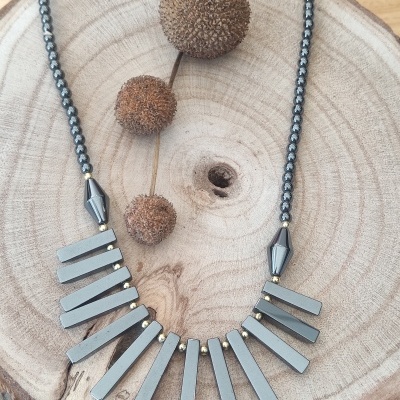 Colar com barras cinzentas e contas pretas sobre madeira com bolas secas