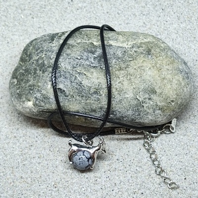 Colar com pendente em forma de camelo com pedra, cordão preto, sobre pedra e areia.