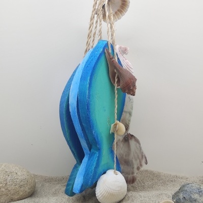 Sino dos ventos azul e verde em forma de peixe com conchas penduradas sobre areia