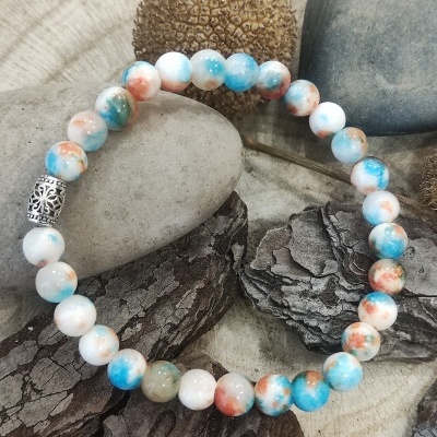 Pulseira de contas coloridas em pedra com detalhe metálico prateado sobre elementos naturais