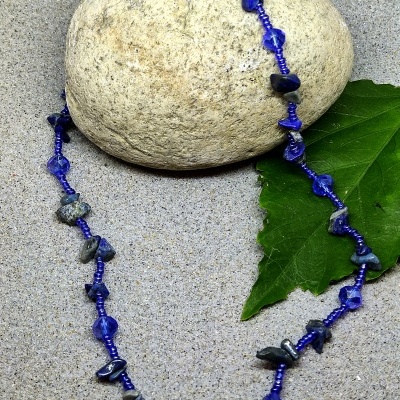 Colar azul com pedras escuras sobre pedra clara e folha verde