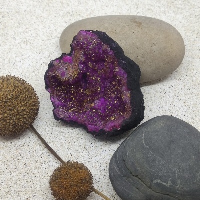 Geodo roxo com pedras lisas e planta seca sobre superfície clara.