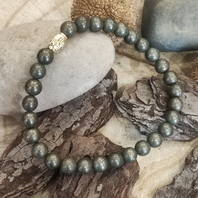 Pulseira de contas cinzentas e uma conta dourada sobre madeira com cascas e pedras