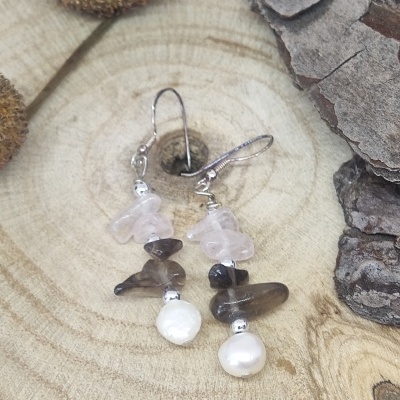 Brincos pendentes com pedras rosa e castanhas e pérola sobre madeira clara com casca e sementes