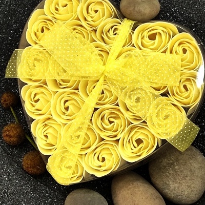 Caixa em forma de coração com flores amarelas decorativas e fita amarela, rodeada por pedras