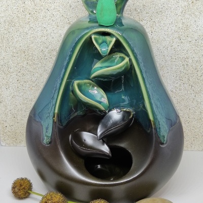 Fonte decorativa de cerâmica em forma de pêra verde e castanha com folhas interiores e elementos naturais ao lado