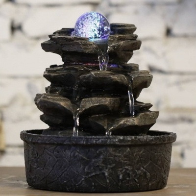 Fonte de água decorativa com esfera luminosa azul e estrutura de rochas artificiais escuras.