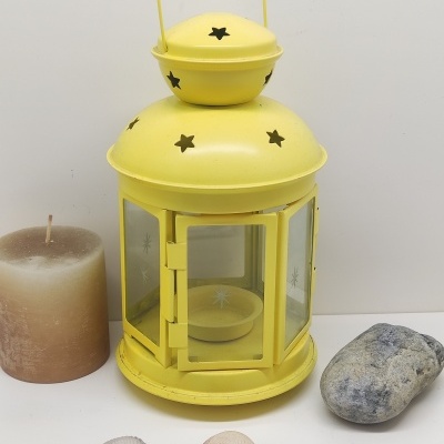 Lanterna metálica amarela com decoração de estrelas e vela castanha em fundo branco