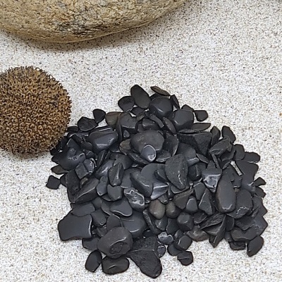 Pequenas pedras pretas em superfície clara com pedras grandes ao fundo