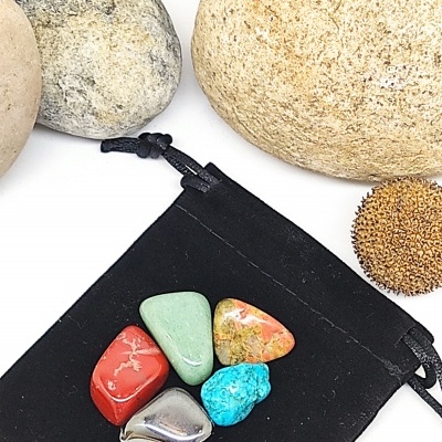 Pedras polidas coloridas sobre bolsa preta com pedras naturais ao fundo