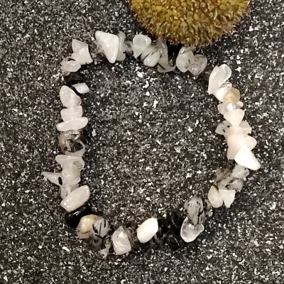 Pulseira de pedras brancas, pretas e bege sobre superfície cinzenta com flor amarela