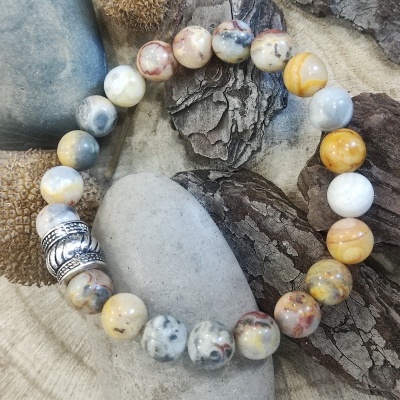 Pulseira de contas marmoreadas bege e cinza com elementos metálicos sobre pedras e casca de árvore