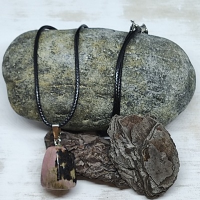 Colar com pendente de pedra rosada e cordão preto sobre pedra cinzenta e casca seca