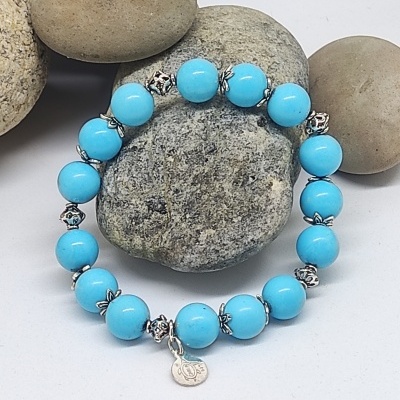 Pulseira azul com contas redondas e elementos metálicos sobre pedras decorativas