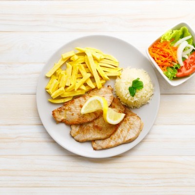 Prato com peixe grelhado, batatas fritas, arroz e salada numa mesa de madeira clara