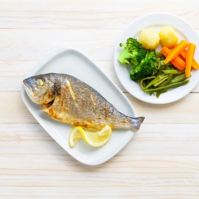 Prato com peixe grelhado e legumes cozidos sobre mesa de madeira clara