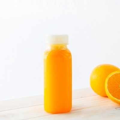 Garrafa de sumo de laranja e laranjas numa mesa clara