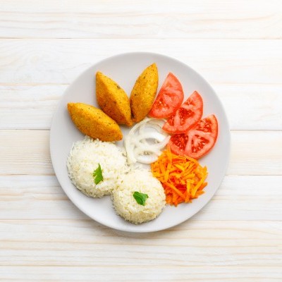 Prato com bolinhos, arroz, tomate, cebola e cenoura sobre mesa clara