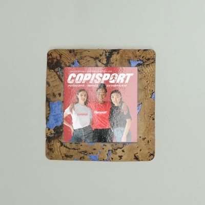 Moldura quadrada de cortiça com manchas azuis contendo uma foto de três mulheres com t-shirts da COPISPORT