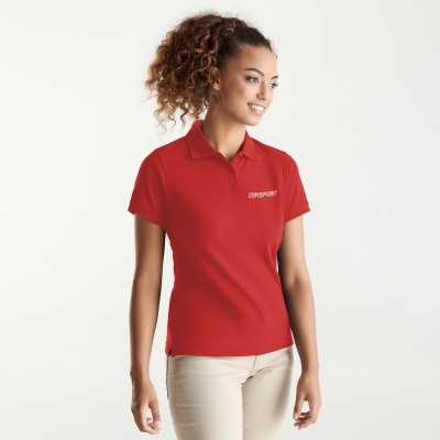 Mulher com t-shirt polo vermelha com texto CORRSPORT e calças bege, fundo branco