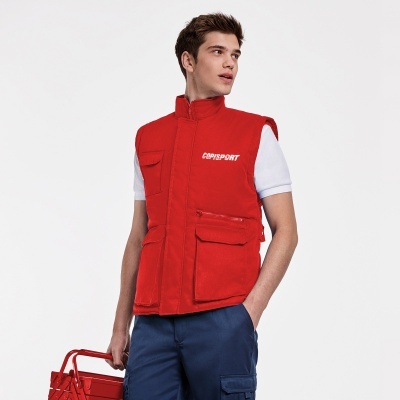 Homem com colete vermelho acolchoado e calças azuis segurando caixa vermelha