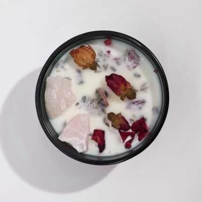 Vela aromática com pétalas de flores secas e cristais em recipiente preto