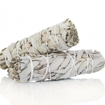 Dois maços de sálvia seca amarrados com fio branco sobre superfície branca