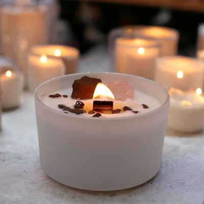 Vela aromática branca em recipiente opaco branco com pedras decorativas e chama acesa