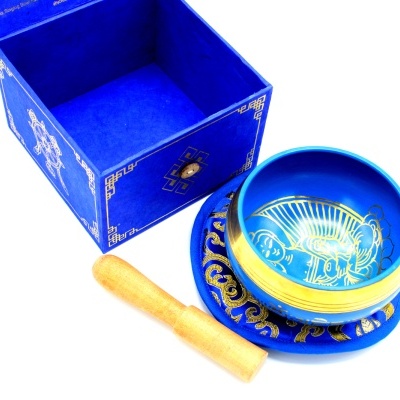 Tigela tibetana azul e dourada com suporte e bastão de madeira, ao lado de caixa azul aberta.