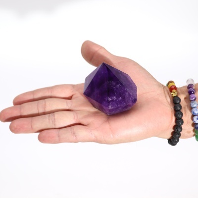 Mão com pulseiras segurando um cristal de ametista roxo facetado